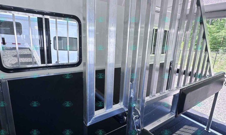 Interior of a metal trailer with vertical stalls and a lowered ramp, windowed side panel visible.