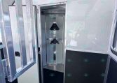 Interior of a metal trailer with an open doorway and a narrow vertical storage rack featuring two black wedge-shaped mounts; metal walls and black flooring visible.