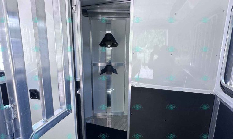Interior of a metal trailer with an open doorway and a narrow vertical storage rack featuring two black wedge-shaped mounts; metal walls and black flooring visible.