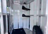 Interior of metal trailer with diamond-plate floor, wall-mounted black fold-down seats, and a spare tire visible at the front.