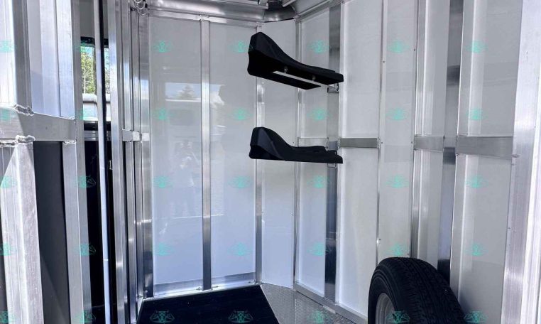 Interior of metal trailer with diamond-plate floor, wall-mounted black fold-down seats, and a spare tire visible at the front.