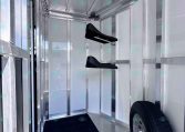 Interior of a aluminum trailered space showing a spare wheel, diamond-plate floor, and a pair of black fold-down saddle racks mounted to the wall, metal walls around.