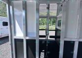 Metal horse trailer interior with partition walls and overhead hooks, viewed toward the rear door. (informative)