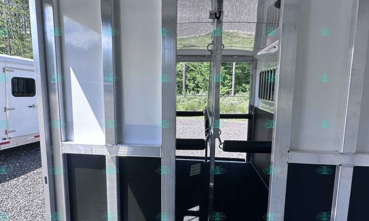 Metal horse trailer interior with partition walls and overhead hooks, viewed toward the rear door. (informative)