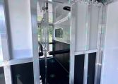 Interior view of an aluminum trailer with partitioned stalls, metal framing, and a row of hooks along the ceiling.
