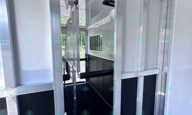 Interior view of an aluminum trailer with partitioned stalls, metal framing, and a row of hooks along the ceiling.