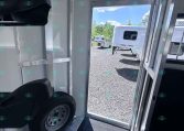 Interior of a silver trailer showing a wheel and diamond-plate floor, with an open door to a gravel lot and other trailers outside