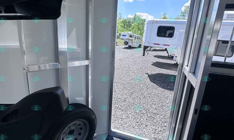 Interior of a silver trailer showing a wheel and diamond-plate floor, with an open door to a gravel lot and other trailers outside