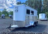 Silver enclosed trailer on a gravel lot with other trailers and pine trees in the background, watermark reads CarolinaTrailersSales.com.
