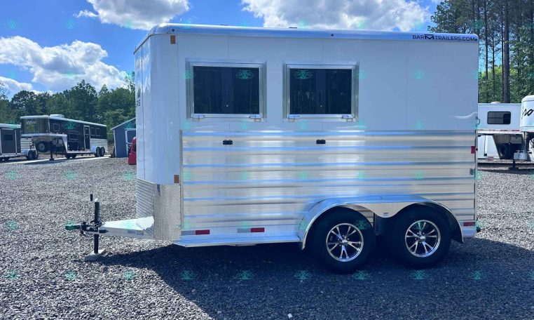 White aluminum trailer with two rectangular windows parked on a gravel lot, other trailers visible in the background.