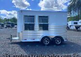 Silver aluminum horse trailer with two front windows and dual axles, parked on a gravel lot at a trailer sales yard.