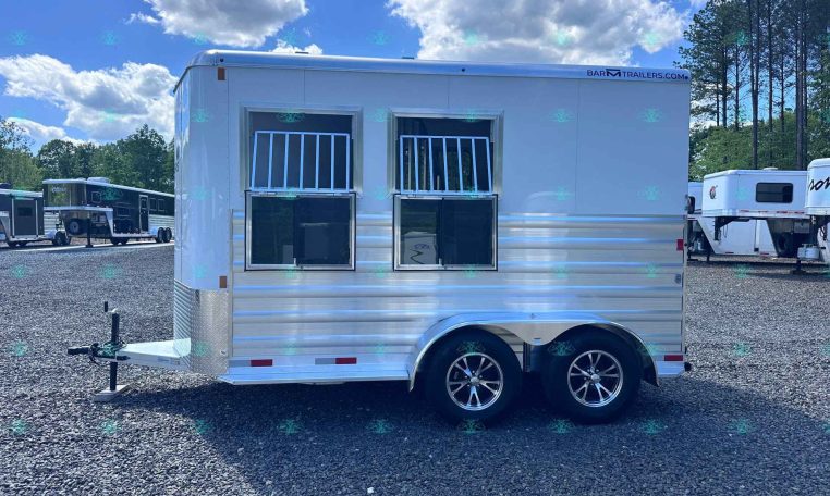 Silver aluminum horse trailer with two front windows and dual axles, parked on a gravel lot at a trailer sales yard.