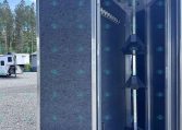 Open aluminum trailer with blue interior walls and a row of metal hooks for hanging gear, viewed from the doorway in a gravel lot.