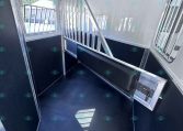 Interior of a horse trailer showing a metal divider, windows, and a black non-slip floor inside a partially partitioned stall.