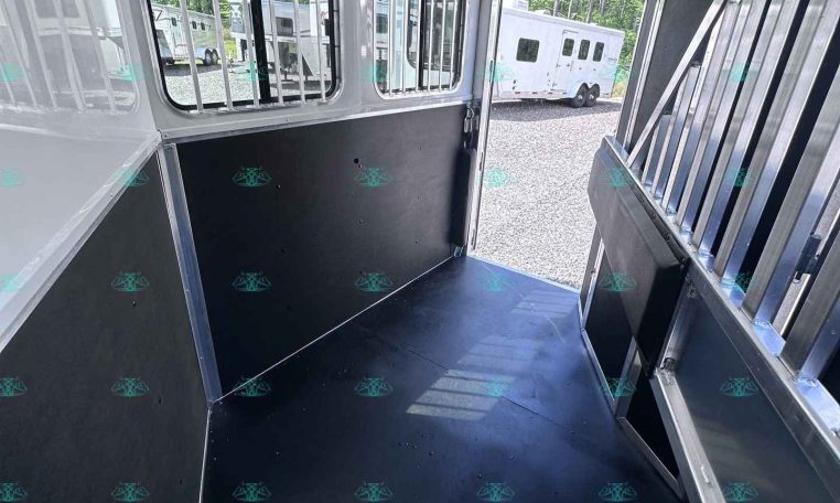 Inside a silver horse trailer with barred windows and black rubber flooring; another trailer is visible outside.