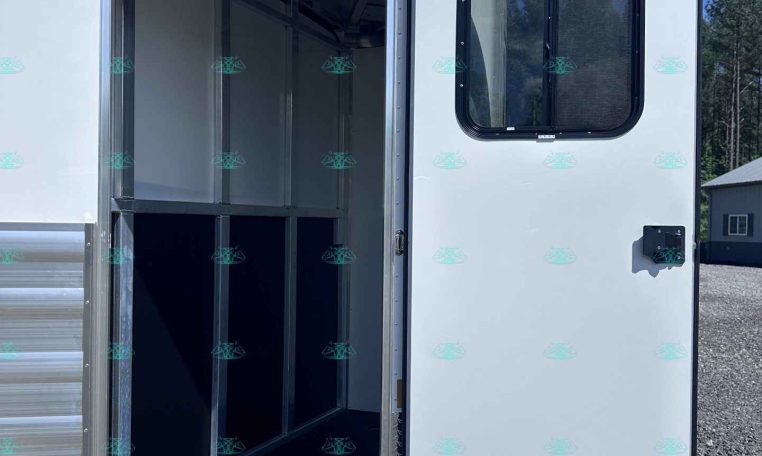 Open horse trailer door revealing empty interior stalls with metal partitions and overhead hooks.