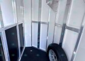 Interior of a silver aluminum cargo trailer with metal framing, wheel mounted in the corner and a spare tire visible on the floor.