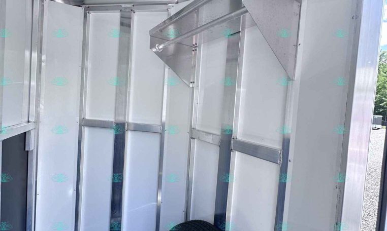 Inside view of a silver enclosed trailer with metal walls, framing, and a visible tire at the floor corner.