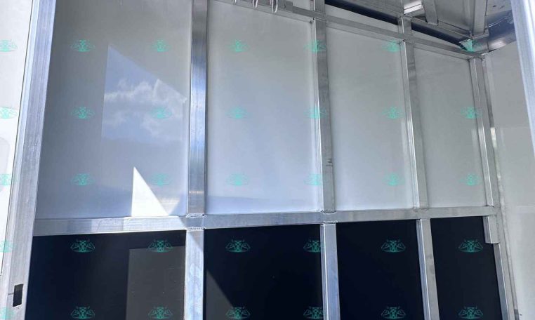 Interior of an aluminum trailer showing metal partitions and a row of hanging hooks inside.