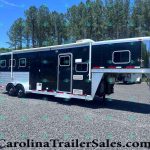 Black and silver horse trailer on a gravel lot with a wooded backdrop and blue sky behind it.