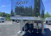 Shiny silver horse trailer with 'EXISS' logo, reflecting trees and blue sky, parked on gravel.
