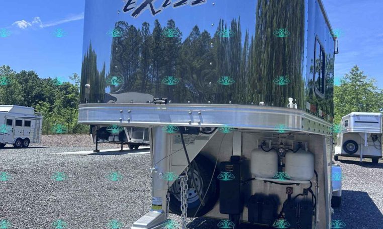 Shiny silver horse trailer with 'EXISS' logo, reflecting trees and blue sky, parked on gravel.