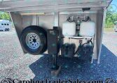 Front storage bay of a travel trailer with a spare tire, two propane tanks, and battery boxes; visible gas lines and gauges.