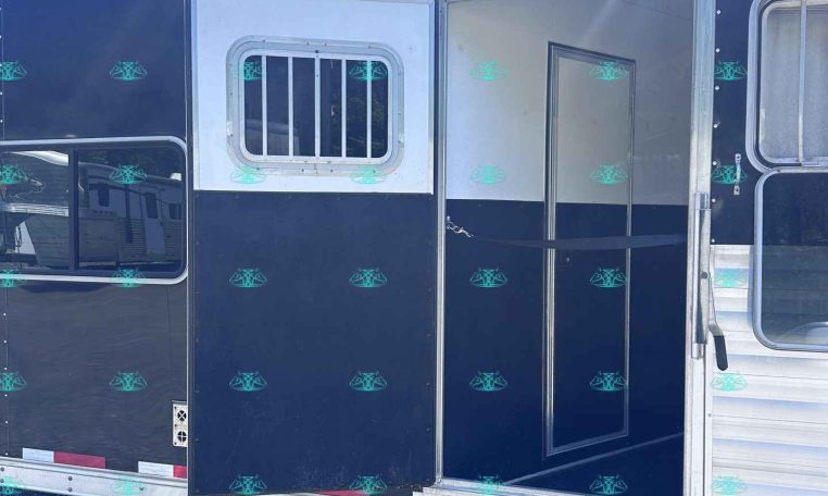 Dark blue trailer side with an open doorway and a small barred window, silver trim, parked on gravel.