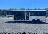 Two-axle dark blue horse trailer with a white roof and silver trim parked on a gravel lot, with trees and a clear blue sky in the background.