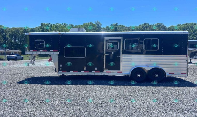 Two-axle dark blue horse trailer with a white roof and silver trim parked on a gravel lot, with trees and a clear blue sky in the background.
