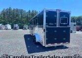 Rear view of a large blue and silver enclosed trailer in a gravel lot, with other trailers and tall trees in the background. Watermark text CarolinaTrailerSales.com across the bottom.