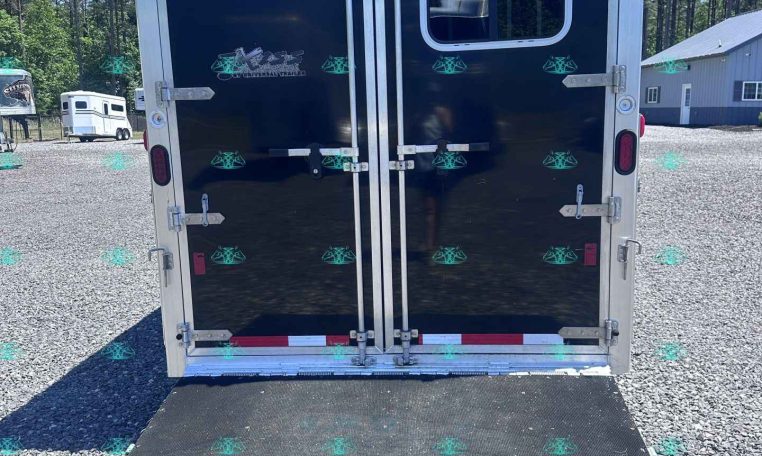 Rear view of a dark blue cargo trailer with large double doors, a lowered ramp, and a small window on the right door in a sunny gravel lot.