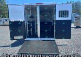 Open horse trailer with ramp down, showing interior stalls and tack area against a gravel lot and blue sky.