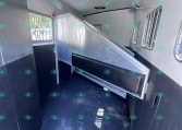 Interior of a metal horse trailer with a divider and barred windows, showing the parking ramp built into the stall area, and ceiling vents/speakers above.