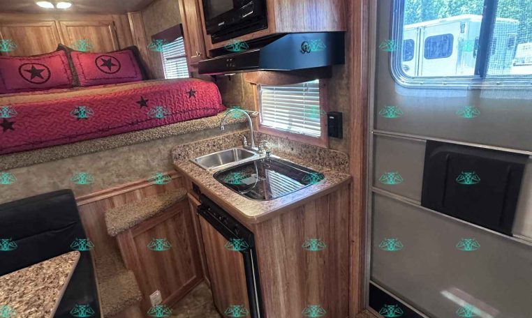 RV interior with a bed and pink quilt, built-in wood cabinets, microwave, and small kitchen with stove and sink.