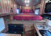 Interior of a compact trailer with a pink bed at the far end and wooden cabinets along the walls