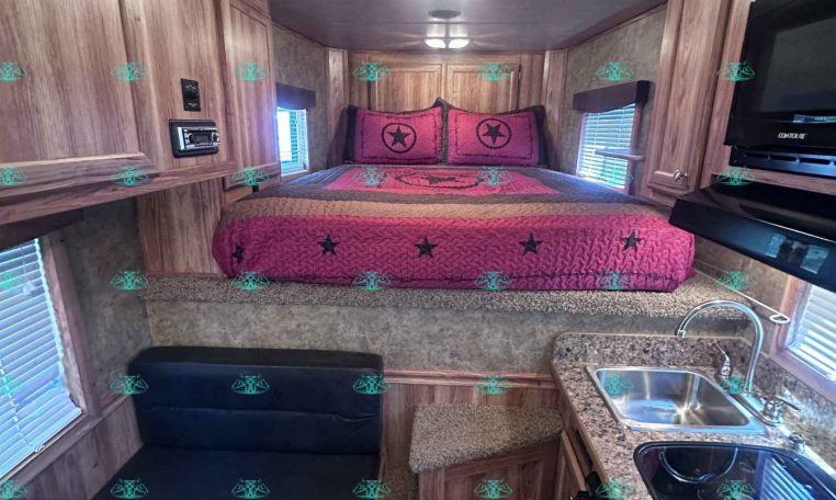 Interior of a compact trailer with a pink bed at the far end and wooden cabinets along the walls