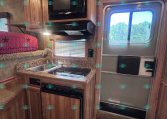 RV kitchen with wood cabinets, microwave above the stove, and a countertop sink area under a window.