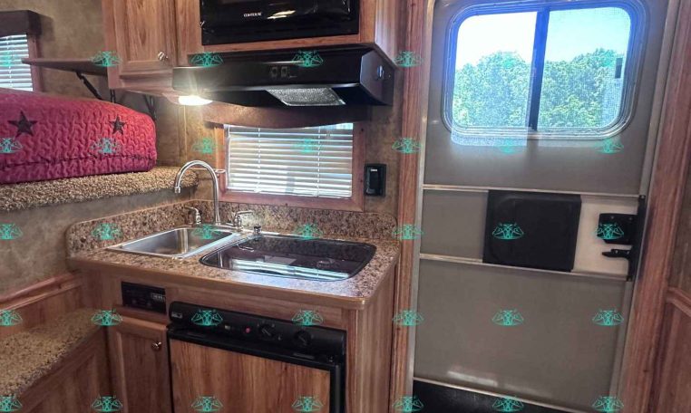 RV kitchen with wood cabinets, microwave above the stove, and a countertop sink area under a window.