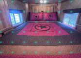 Interior of a cozy trailer bedroom with a pink quilt and matching star pillows on a bed against wooden cabinets.