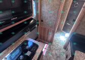 Interior of a bunk trailer kitchen with black microwave and stove, granite countertop, and wooden cabinets.