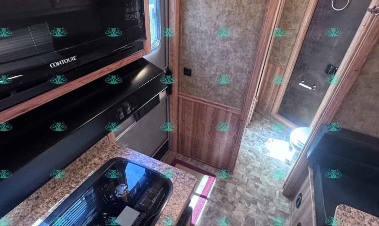 Interior of a bunk trailer kitchen with black microwave and stove, granite countertop, and wooden cabinets.