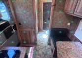 RV kitchen with brown wood cabinets, speckled countertops, and a doorway at the far end with a framed panel and towel ring.