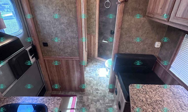 RV kitchen with brown wood cabinets, speckled countertops, and a doorway at the far end with a framed panel and towel ring.