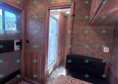 Interior of a wood-panel RV kitchen and seating area with cabinets, a window, and doorway to a bathroom or outside area.