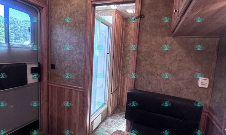 Interior of a wood-panel RV kitchen and seating area with cabinets, a window, and doorway to a bathroom or outside area.