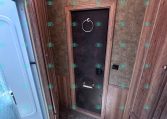 RV bathroom with a frosted shower door on the left, dark central access door with a circular towel ring, and wood paneling.