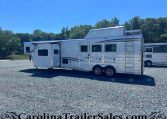 White fifth-wheel RV trailer parked on a gravel lot with trees in the background; dealership watermark at bottom.