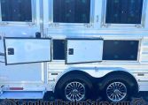 Side view of a silver trailer with open storage compartments and chrome wheels; CarolinaTrailerSales.com visible at the bottom.
