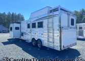 White horse trailer with an open side door and ladder, parked on a gravel lot with trees in the background.
